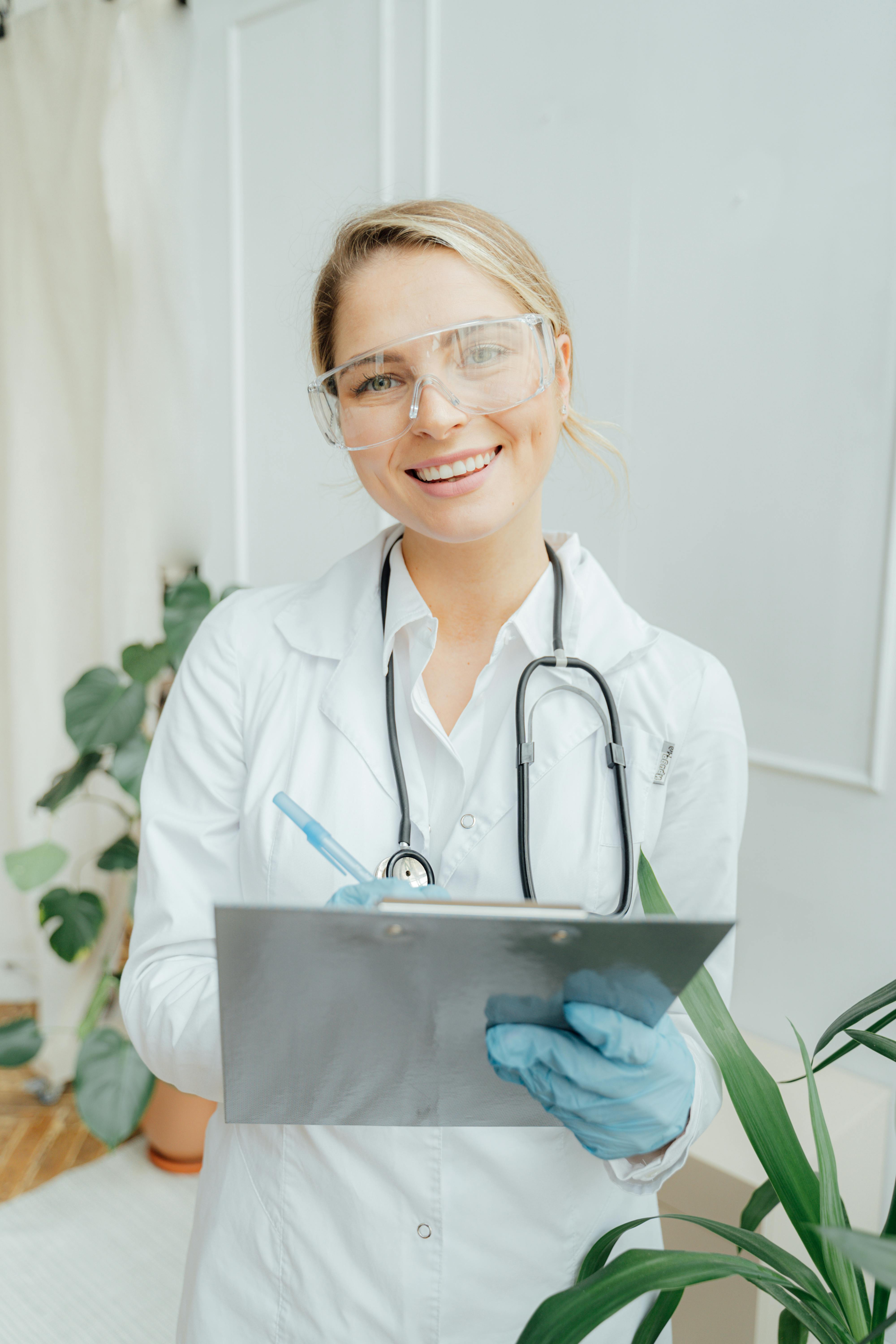 Doctor holding a clipboard and smiling in a bright clinical setting.